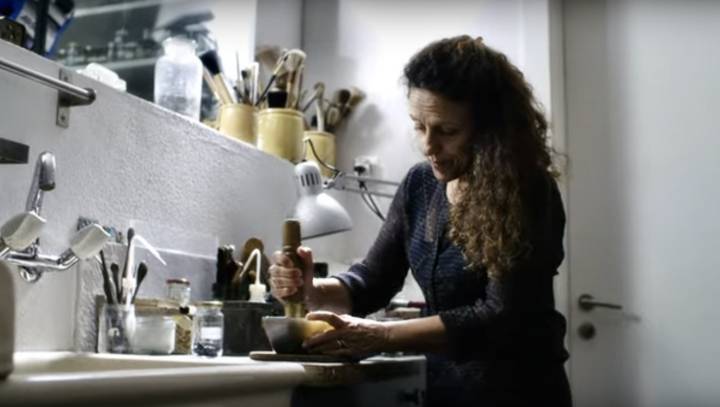 Anita Porchet prepara todos sus esmaltes a mano en su estudio. Se la ve aquí triturando vidrio coloreado con un mazo para obtener partículas parecidas a la arena que, combinadas con una solución acuosa, aplicará a la esfera.