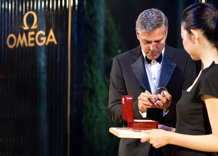 George Clooney autografiando la correa y la caja de presentación del Omega De Ville Hour Vision Annual Calendar que ha estado llevando.